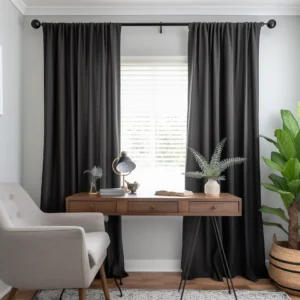 A room with a desk having lamp, a vase along with a sofa and plant pot with black Rod Pocket curtains